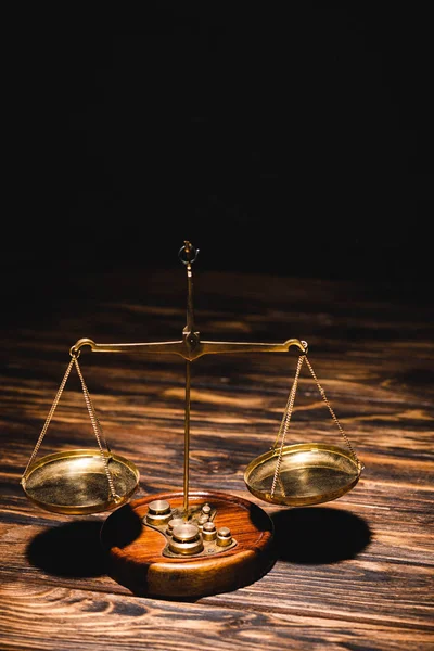Golden scales of justice on wooden table on black background — Stock Photo