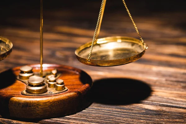 Close up view of golden scales of justice on wooden table on black background — Stock Photo