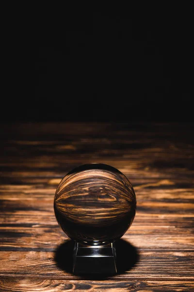 Crystal ball on wooden table on black background — Stock Photo