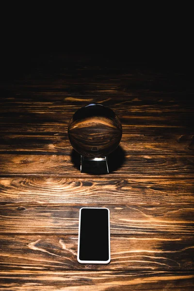 Boule de cristal avec smartphone sur table en bois sur fond noir — Photo de stock