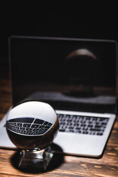 Selective focus of crystal ball near laptop on wooden table on black background — Stock Photo