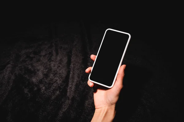 Vista cortada de mulher segurando smartphone com tela em branco no pano de veludo preto — Fotografia de Stock