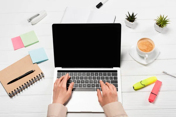 Обрізаний вид жінки, що використовує ноутбук на робочому місці з приладдям для офісу та кавою — стокове фото