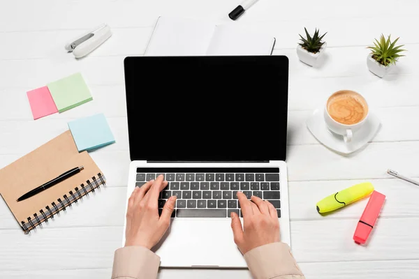 Cropped view of woman using laptop at workplace with office supplies and coffee — Stock Photo