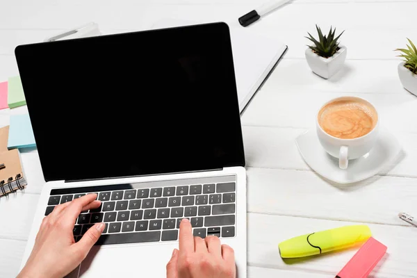 Cropped view of woman using laptop at workplace with office supplies and coffee — Stock Photo