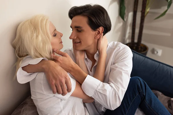 Vista lateral de la pareja joven abrazándose en el sofá en la sala de estar - foto de stock