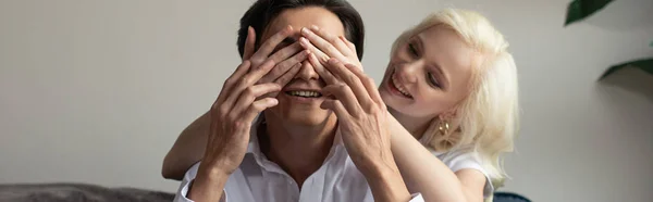 Smiling girl covering eyes to boyfriend at home, panoramic shot — Stock Photo