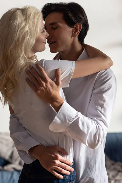 Sorrindo homem abraçando atraente namorada loira em casa — Fotografia de Stock
