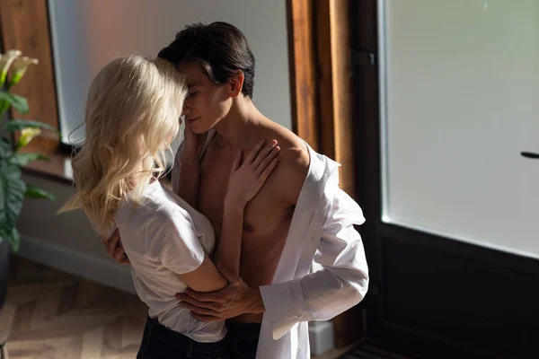 Блондинка обнимает мужчину без рубашки в гостиной — стоковое фото