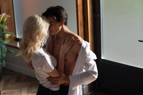 Blonde woman hugging shirtless man in living room — Stock Photo