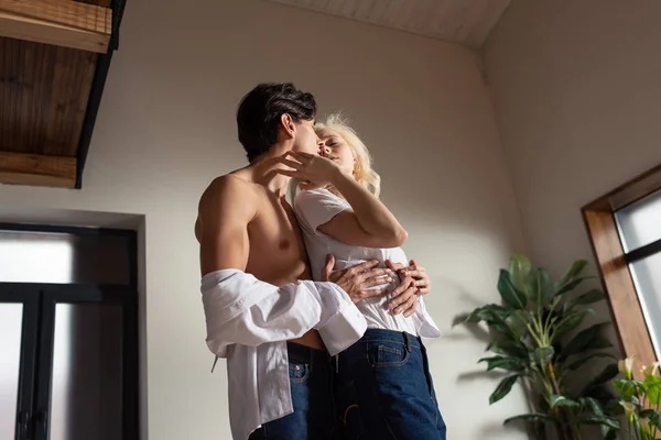 Vista basso angolo di ragazza toccando collo di uomo senza camicia in soggiorno — Foto stock