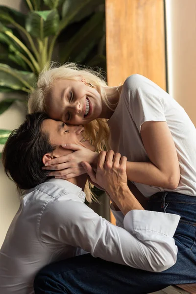 Sonriente pareja joven abrazándose al lado de la ventana en la sala de estar - foto de stock