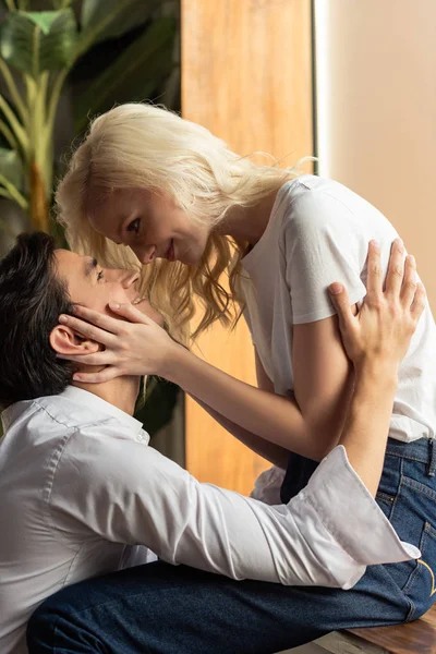 Side view of smiling blonde girl touching boyfriend while sitting on windowsill at home — Stock Photo