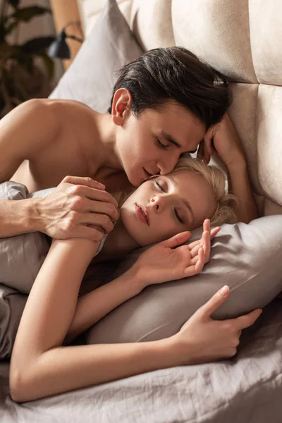 Hombre guapo besando durmiendo novia en la cama - foto de stock