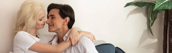 Side view of smiling couple embracing on sofa in living room, panoramic shot — Stock Photo