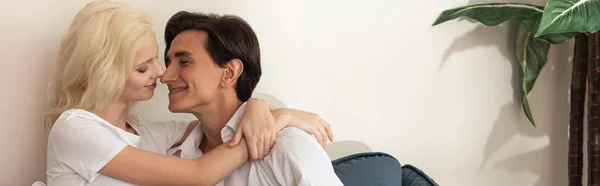 Seitenansicht eines lächelnden Paares, das sich auf dem Sofa im Wohnzimmer umarmt, Panoramaaufnahme — Stockfoto