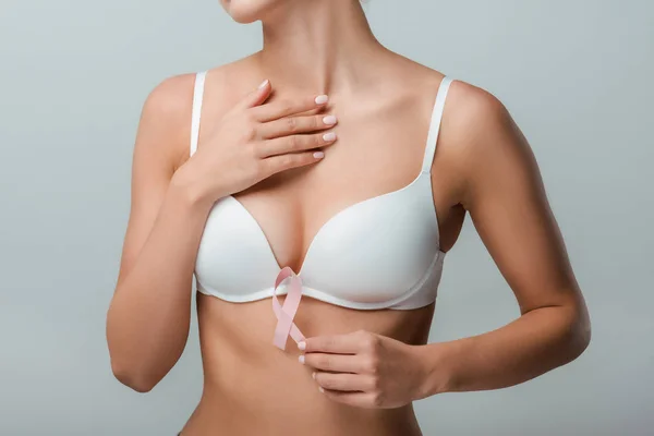 Vue recadrée de fille en soutien-gorge blanc tenant ruban rose comme sensibilisation au cancer du sein isolé sur gris — Photo de stock