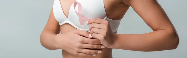 Панорамний знімок жінки в білому бюстгальтері, що тримає рожеву стрічку як обізнаність про рак молочної залози ізольовано на сірому — стокове фото