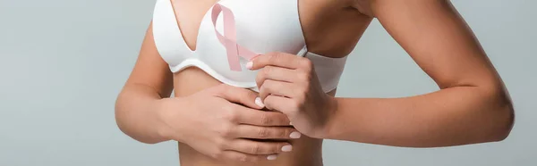 Colpo panoramico di donna in reggiseno bianco che tiene il nastro rosa come consapevolezza del cancro al seno isolato su grigio — Foto stock