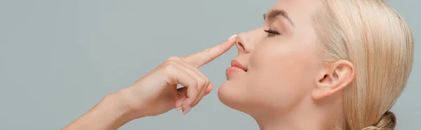 Plan panoramique de femme heureuse touchant le nez isolé sur gris — Photo de stock