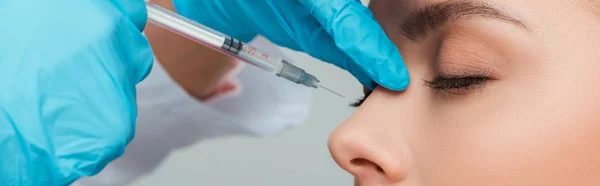 Colpo panoramico di cosmetologo fare l'iniezione di bellezza alla donna attraente isolato su grigio — Foto stock