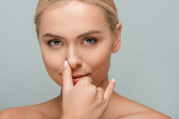 Attractive woman touching nose and looking at camera isolated on grey — Stock Photo