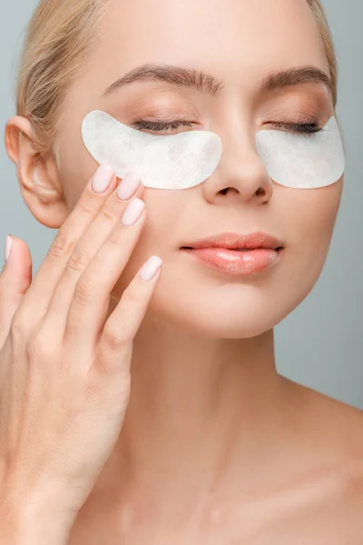 Séduisante femme avec des patchs oculaires touchant le visage isolé sur gris — Photo de stock