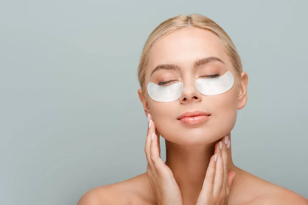 Femme nue avec des patchs pour les yeux touchant le visage isolé sur gris — Photo de stock