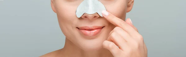 Panoramic shot of happy woman pointing with finger at nose strip isolated on grey — Stock Photo