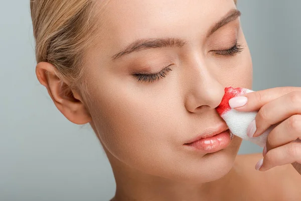 Mujer lesionada sosteniendo vendaje con sangre aislada en gris — Stock Photo