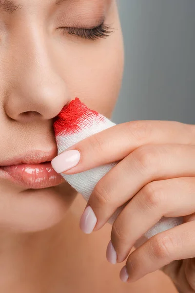 Vue recadrée d'une femme blessée tenant un bandage avec du sang isolé sur du gris — Photo de stock