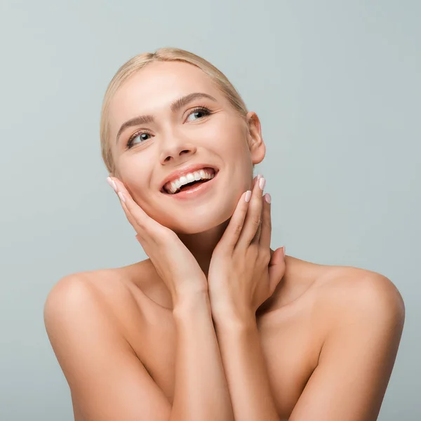 Chica feliz tocando el cuello y sonriendo aislado en gris - foto de stock