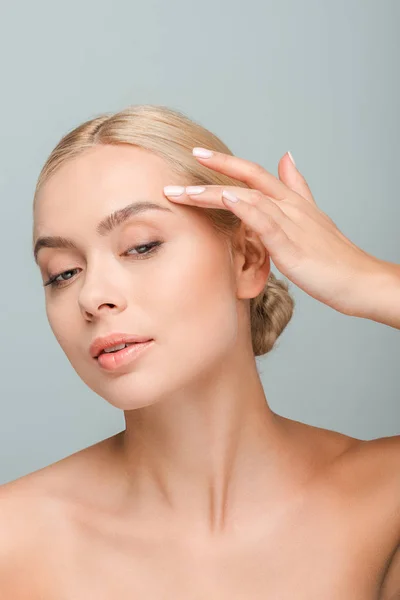 Junge schöne Frau schaut weg und berührt Gesicht isoliert auf grau — Stockfoto