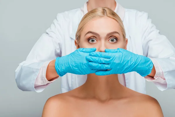 Обрізаний вид косметолога, що закриває рот оголеної жінки ізольовано на сірому — стокове фото