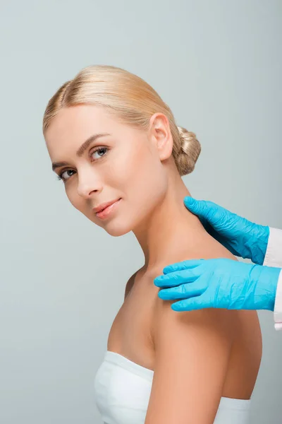 Ausgeschnittene Ansicht einer Kosmetikerin in blauen Latex-Handschuhen, die den Rücken einer Frau berührt, isoliert auf grau — Stockfoto