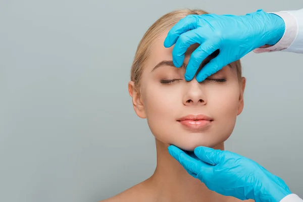 Cropped view of beautician in latex gloves touching nose of naked woman isolated on grey — Stock Photo