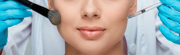 Panoramaaufnahme einer Kosmetikerin in Latexhandschuhen, die Kosmetikbürste und Spritze in der Nähe eines Mädchens hält — Stockfoto