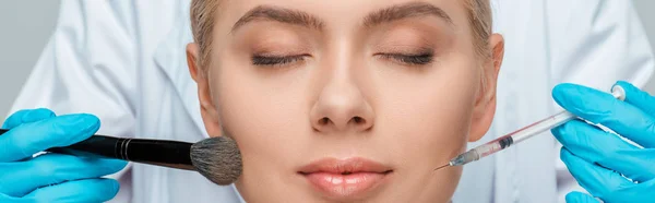 Panoramic shot of beautician in latex gloves holding cosmetic brush and syringe near girl with closed eyes — Stock Photo