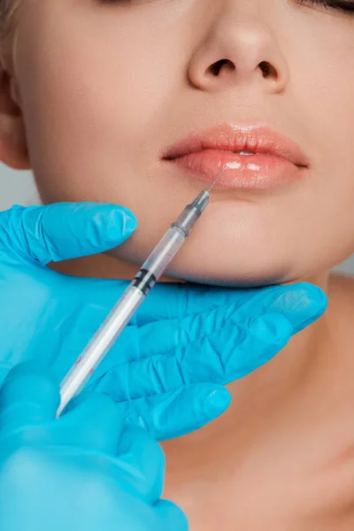 Ausgeschnittene Ansicht einer Kosmetikerin in Latexhandschuhen, die Spritze in der Nähe der Lippen einer Frau hält — Stockfoto