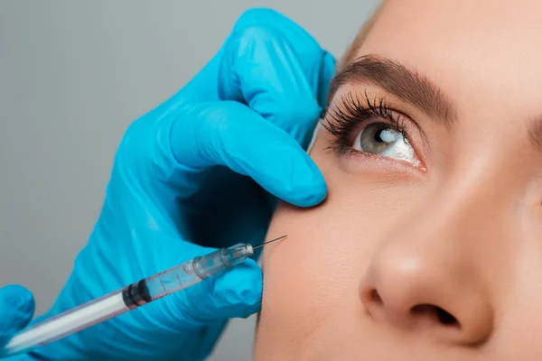 Vista recortada de esteticista en guantes de látex con jeringa cerca de chica aislada en gris - foto de stock