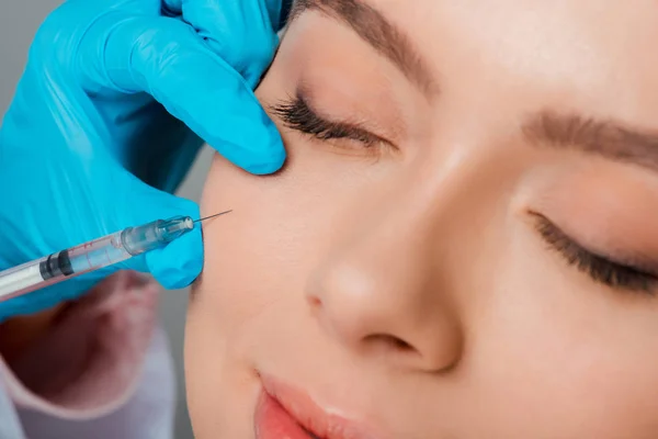 Primer plano de esteticista en guante de látex con jeringa cerca de chica con los ojos cerrados - foto de stock