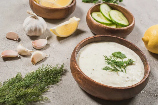 Homemade tzatziki sauce in wooden bowl with ingredients and greenery on stone background — Stock Photo