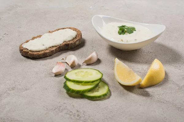 Garlic, lemon and cucumber slices with tzatziki sauce on stone surface — Stock Photo