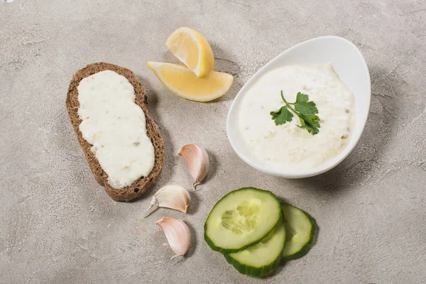 Top view of tzatziki sauce with raw ingredients and bread on stone background — Stock Photo