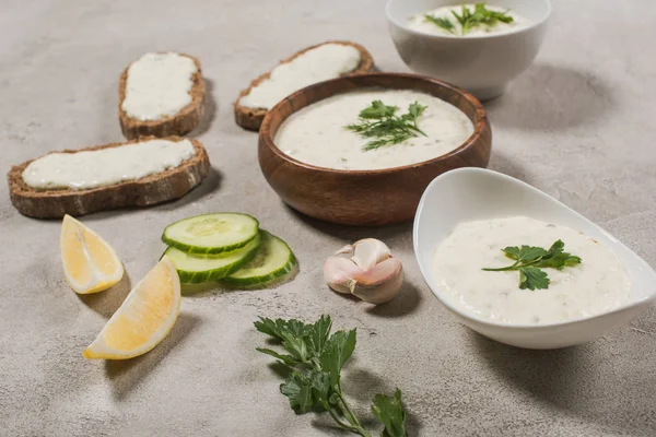 Tzatziki sauce in bowls with raw ingredients on stone background — Stock Photo
