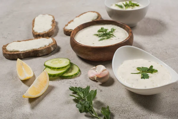 Salsa tzatziki in ciotole con materie prime su fondo pietra — Foto stock