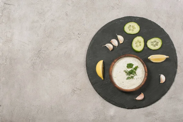 Vista superior de la salsa tzatziki con rodajas de verduras y limón a bordo sobre fondo de piedra - foto de stock