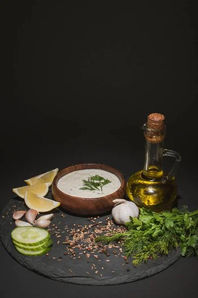 Tzatziki sauce with organic ingredients, spices and olive oil on dark board on black background — Stock Photo