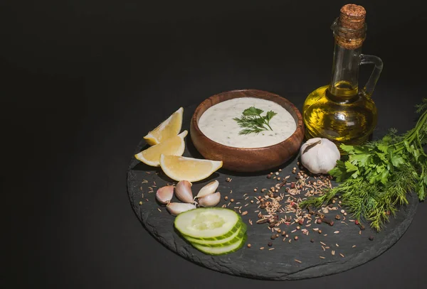 Tzatziki sauce with organic ingredients, spices and olive oil on dark board on black background — Stock Photo