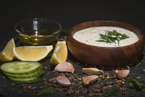 Foco seletivo de molho tzatziki com especiarias e ingredientes em fundo preto — Fotografia de Stock